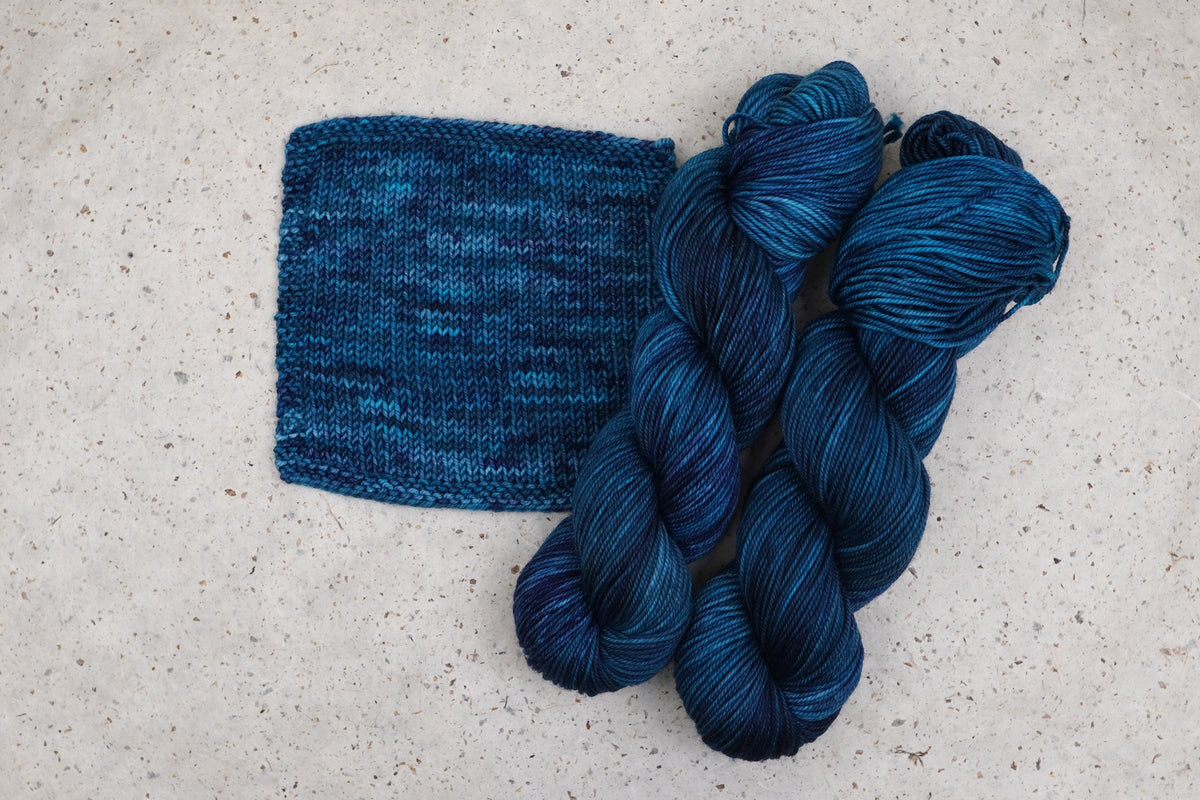 Wild Woollys Teal of Fortune yarn in deep teal and blue, two skeins with a knitted swatch