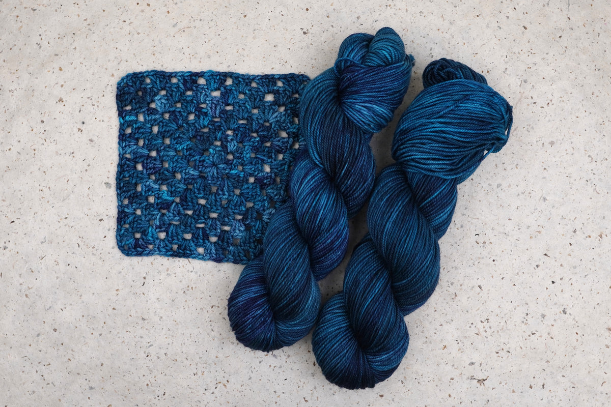 Wild Woollys Teal of Fortune yarn in deep teal and blue, two skeins with a crocheted swatch