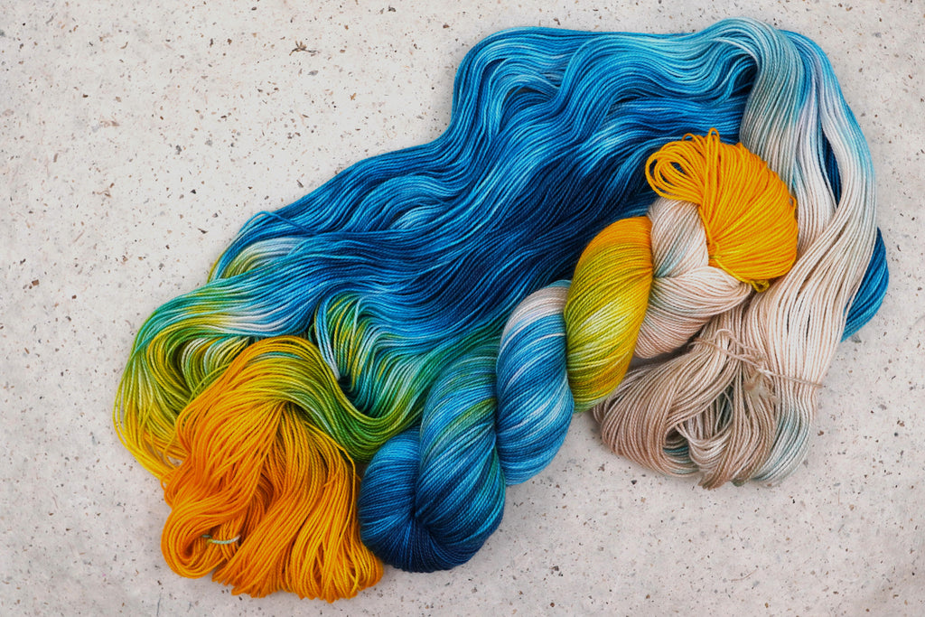 Hilo Tropical Escape de Wild Woollys — una madeja abierta en amarillo dorado, crema, verde azulado y azul océano
