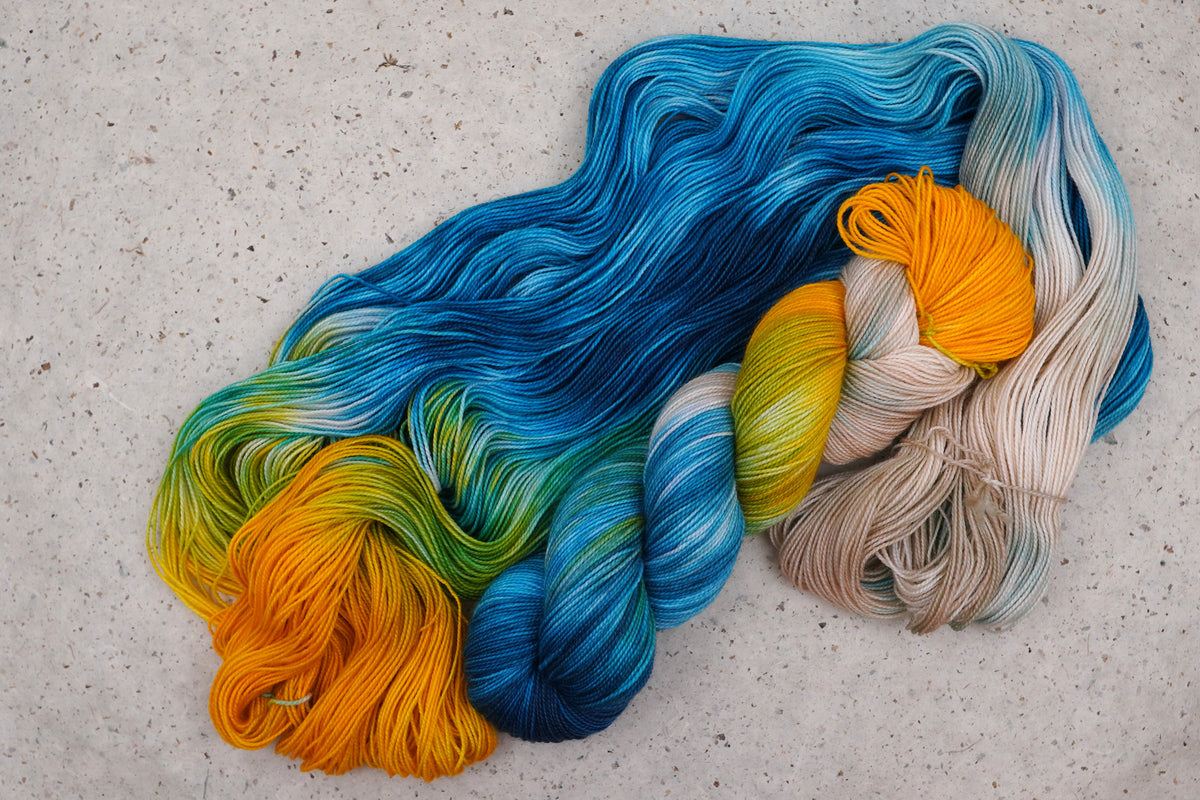 Wild Woollys Tropical Escape yarn, an unwound skein showing golden yellow, cream, teal, and ocean blue