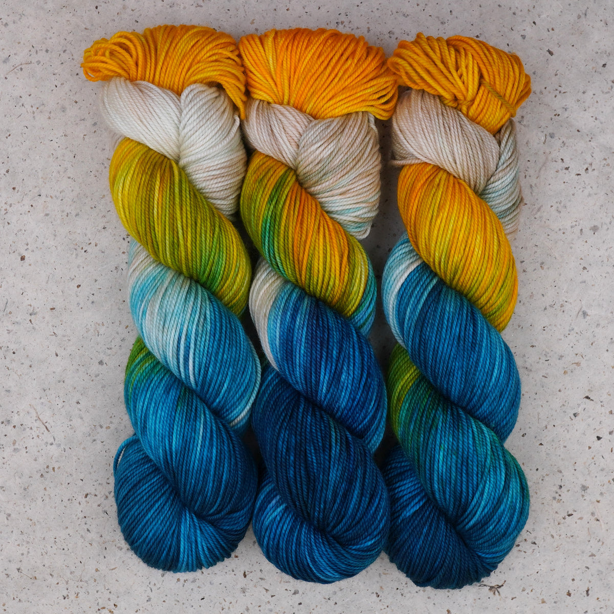 Wild Woollys Tropical Escape DK yarn, three skeins in golden yellow, cream, teal, and ocean blue