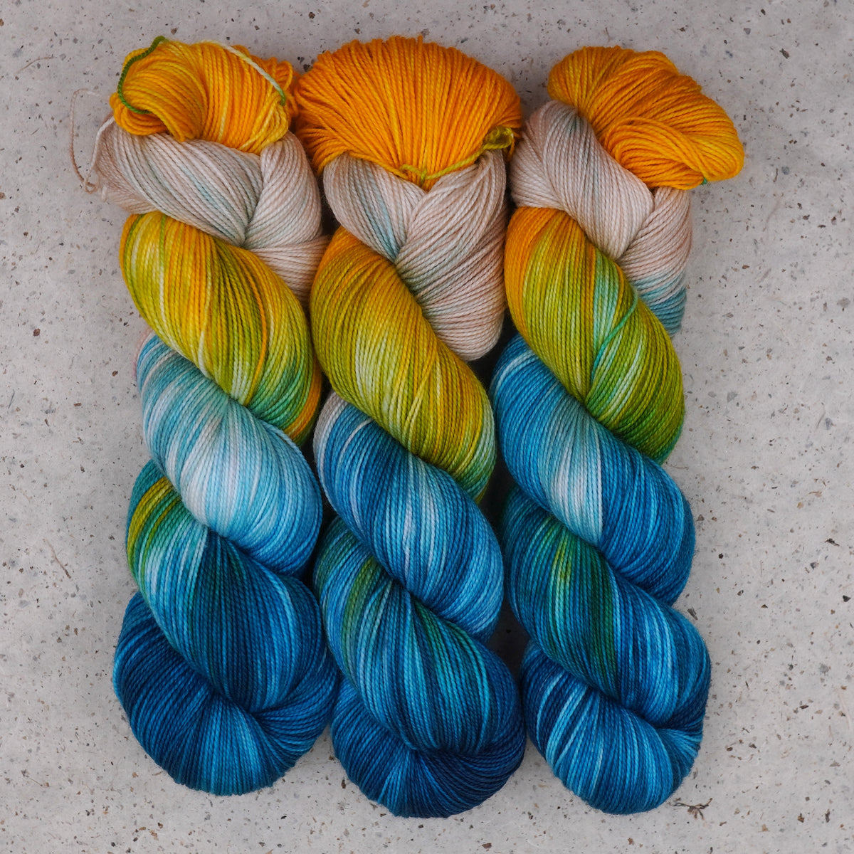 Wild Woollys Tropical Escape Fingering yarn, three skeins in golden yellow, cream, teal, and ocean blue