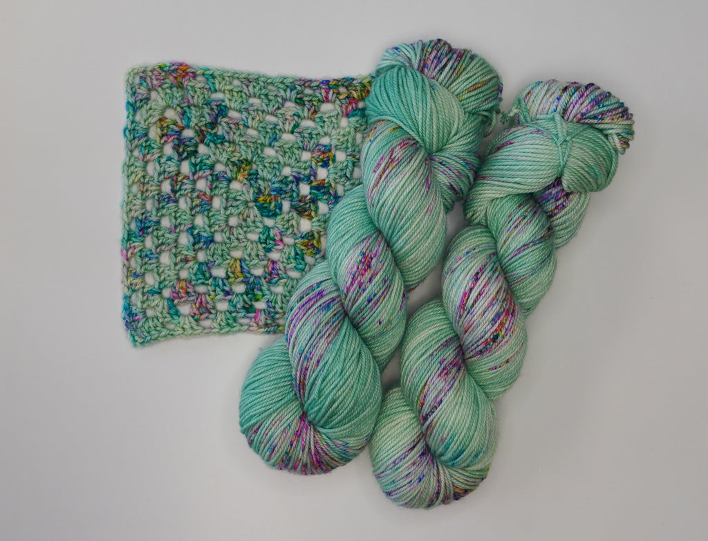 Wild Woollys Undersea Garden yarn, two skeins and a crocheted swatch in teal with colorful speckles