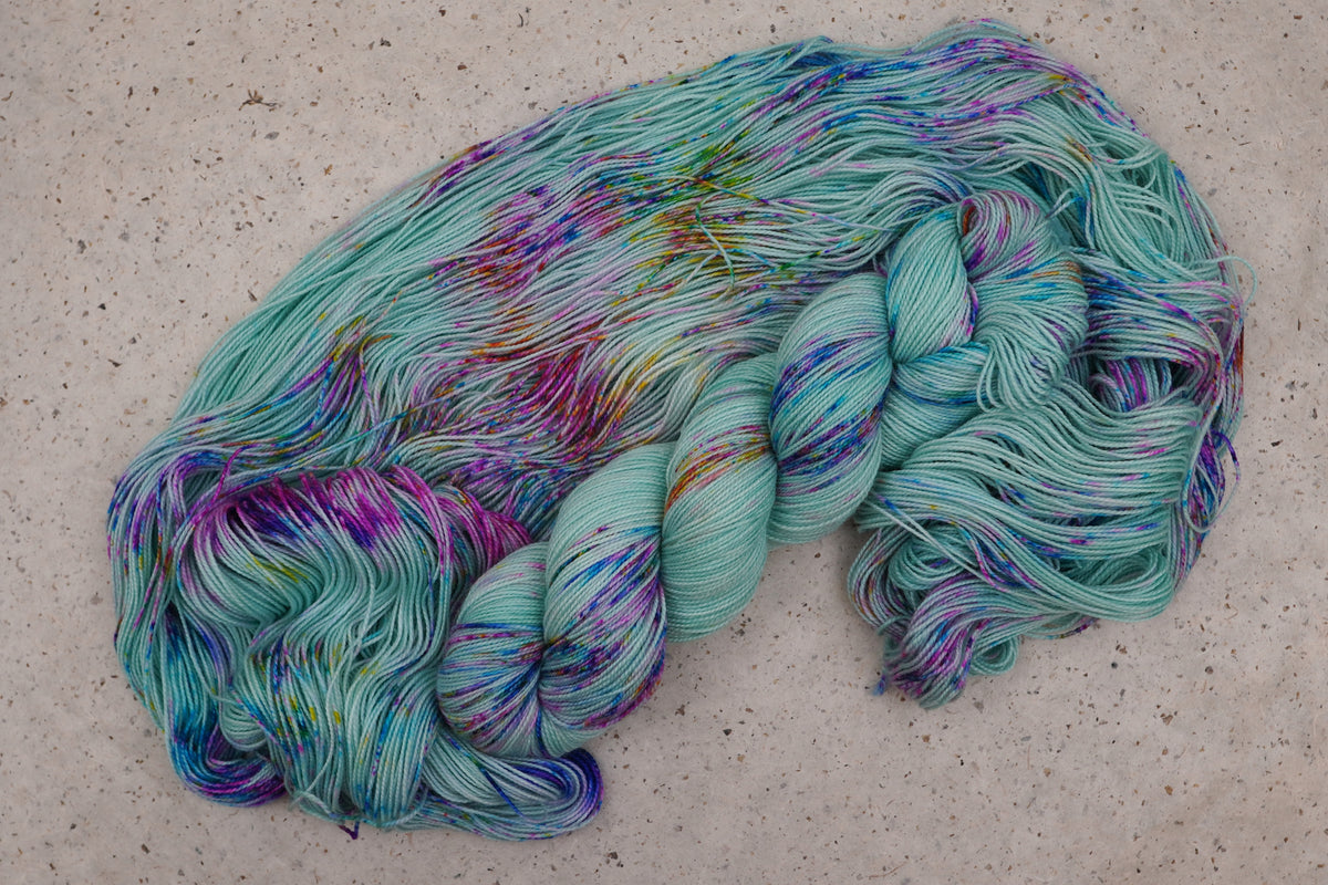 Wild Woollys Undersea Garden yarn, an unwound skein showing soft mint green with purple and blue speckles