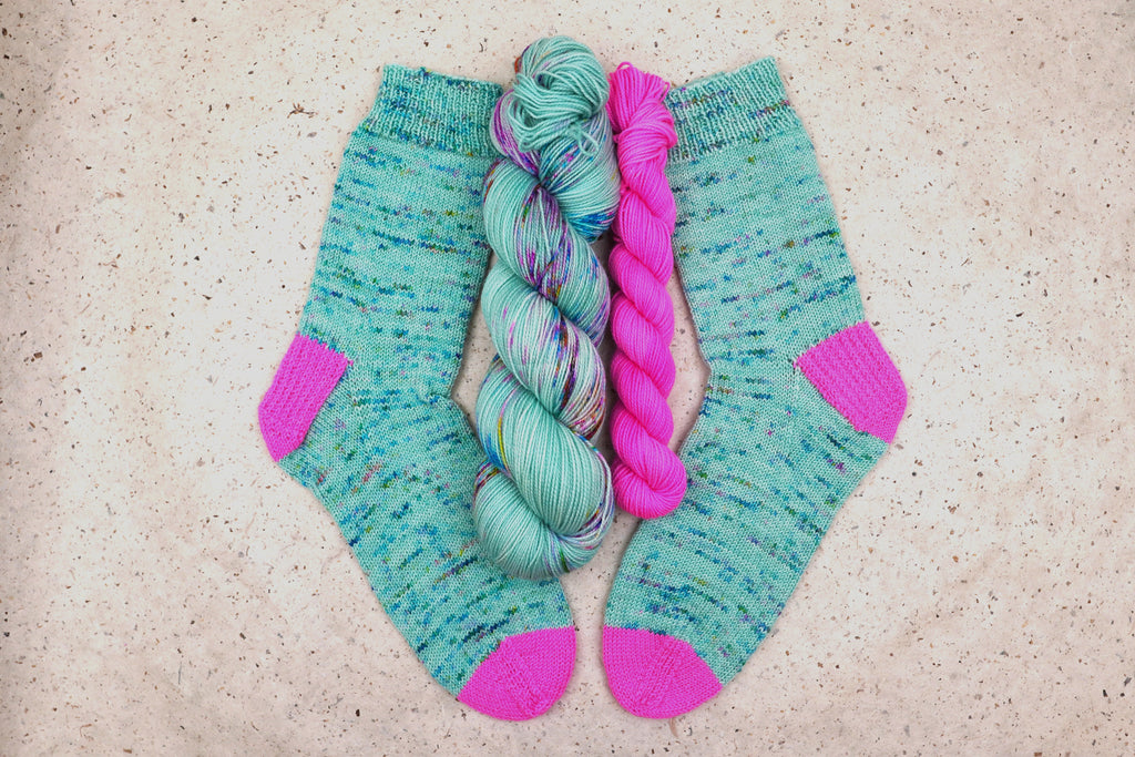 Hand-knit socks in Wild Woollys Undersea Garden with contrasting hot pink heels and toes, shown with the sock set skeins