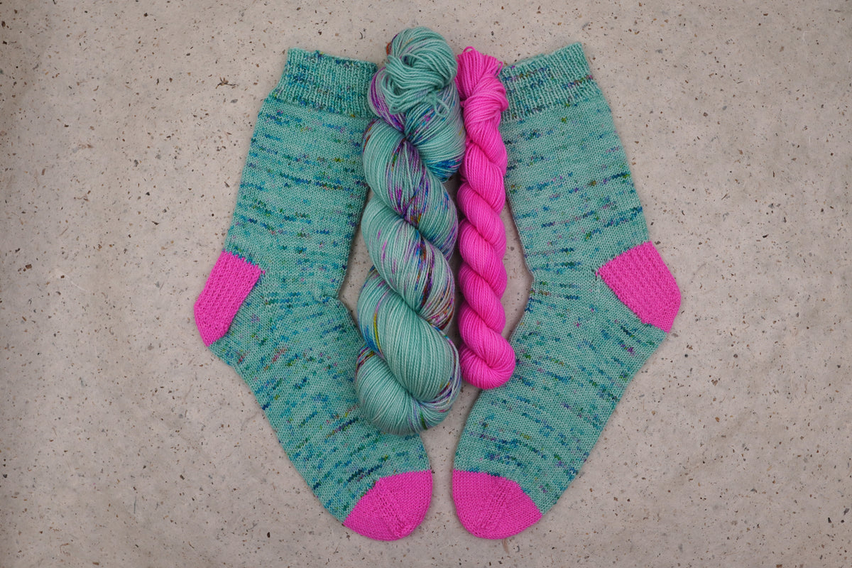 Hand-knit socks in Wild Woollys Undersea Garden with contrasting hot pink heels and toes, shown with the sock set skeins
