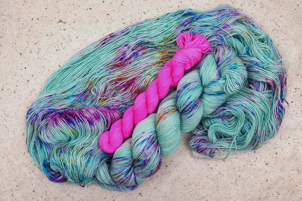 Wild Woollys Undersea Garden sock set, an unwound skein in soft mint green with purple and blue speckles with a contrasting hot pink mini-skein