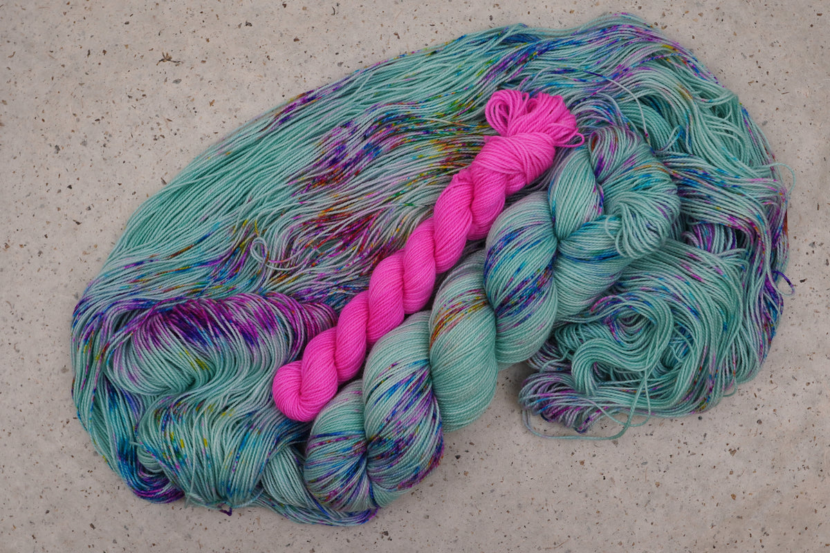 Wild Woollys Undersea Garden sock set, an unwound skein in soft mint green with purple and blue speckles with a contrasting hot pink mini-skein