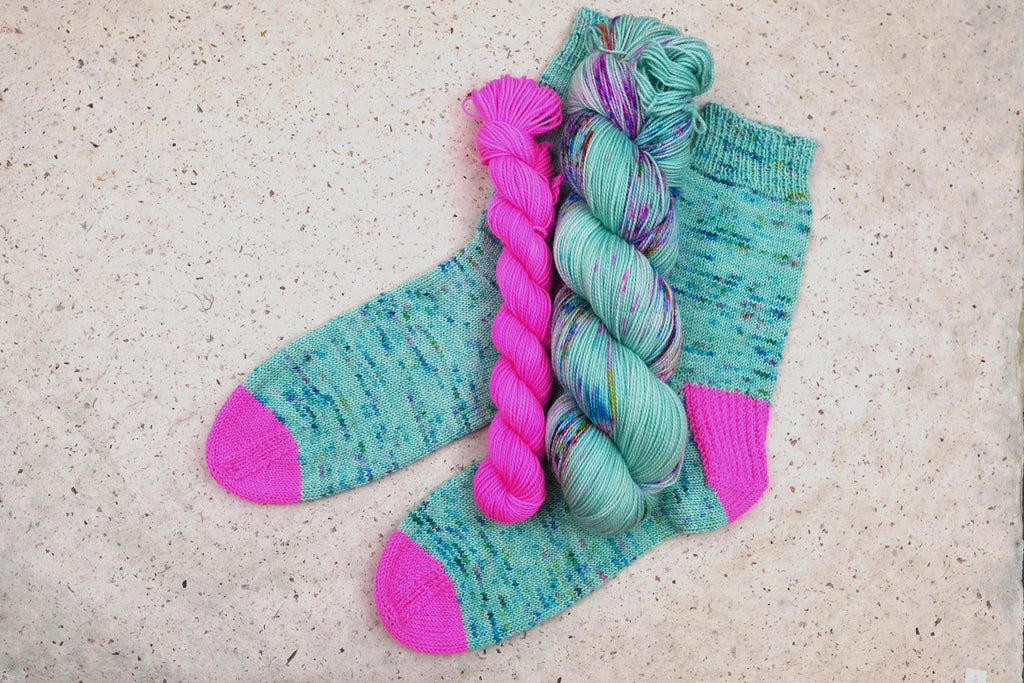 Hand-knit socks in Wild Woollys Undersea Garden with contrasting hot pink heels and toes, shown with the sock set skeins