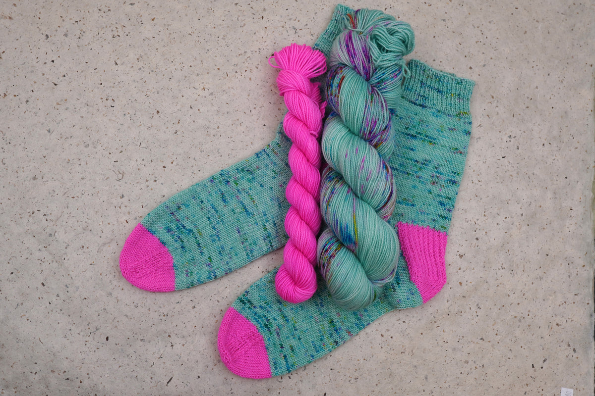 Hand-knit socks in Wild Woollys Undersea Garden with contrasting hot pink heels and toes, shown with the sock set skeins