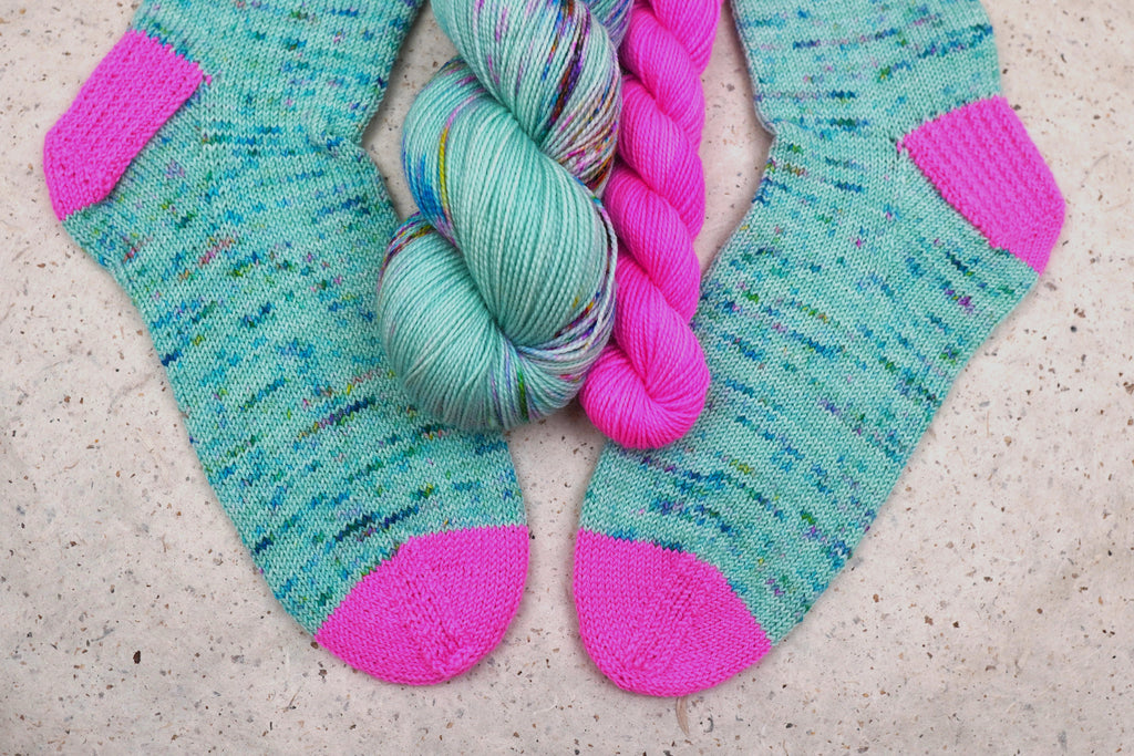 Hand-knit socks in Wild Woollys Undersea Garden with contrasting hot pink heels and toes, shown with the sock set skeins