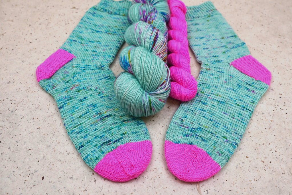 Hand-knit socks in Wild Woollys Undersea Garden with contrasting hot pink heels and toes, shown with the sock set skeins