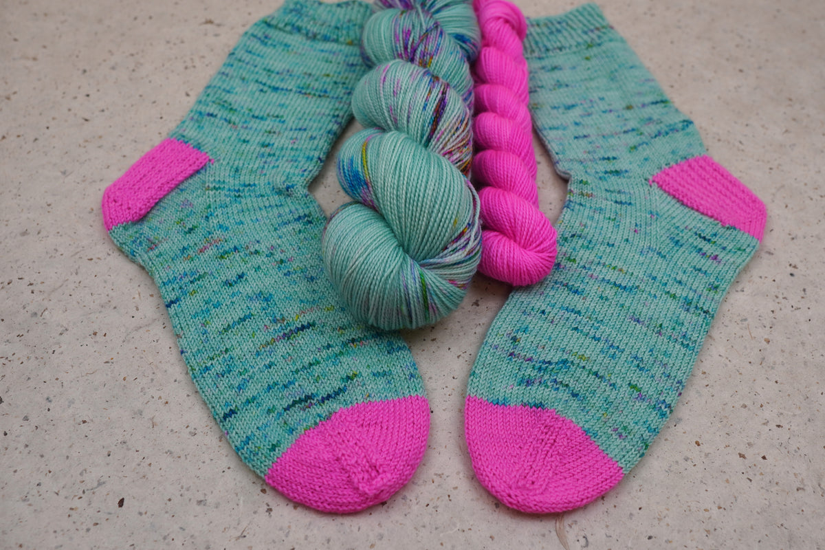 Hand-knit socks in Wild Woollys Undersea Garden with contrasting hot pink heels and toes, shown with the sock set skeins