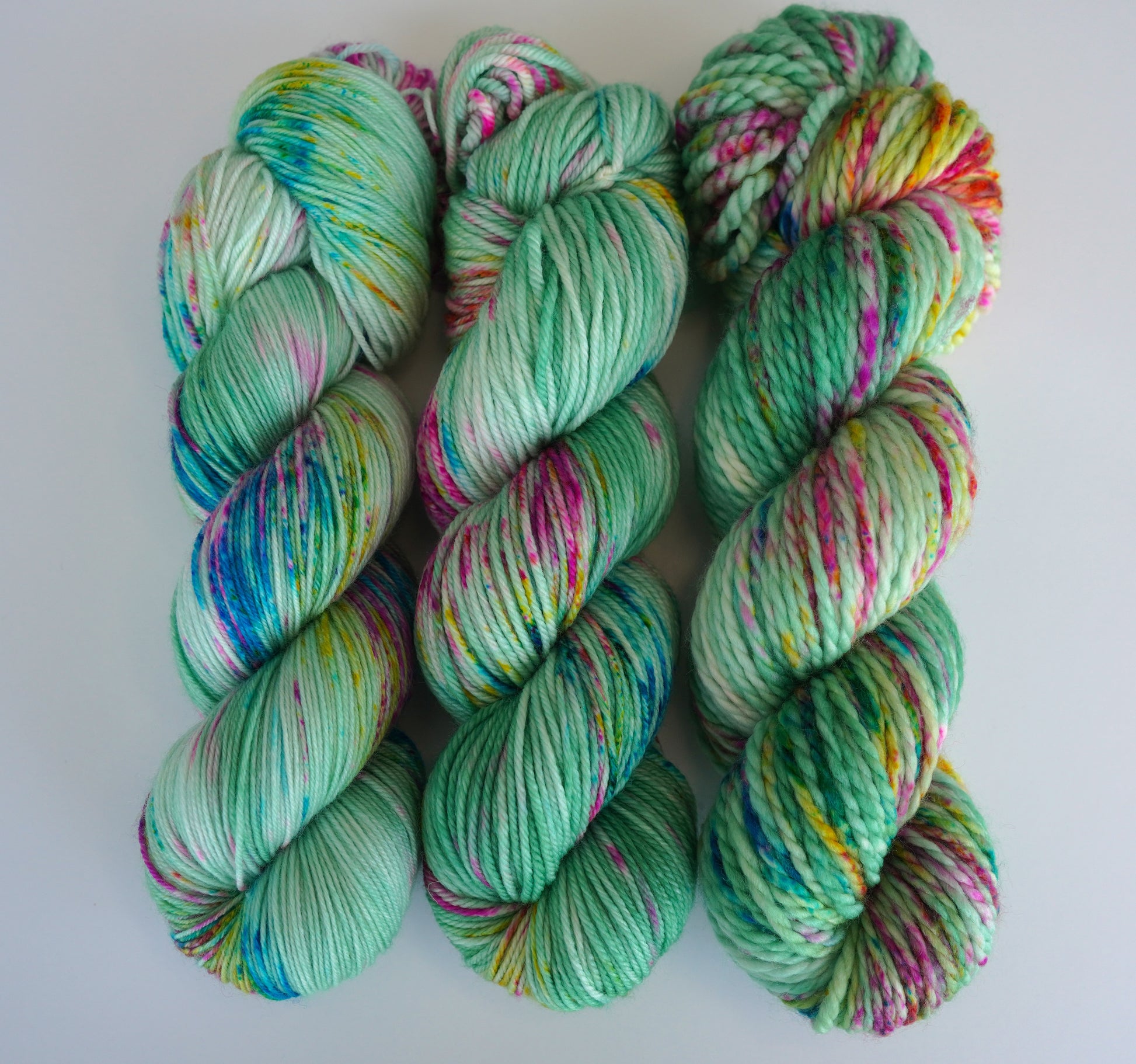 Three skeins of multicolored yarn in varying shades of green with speckles of other colors