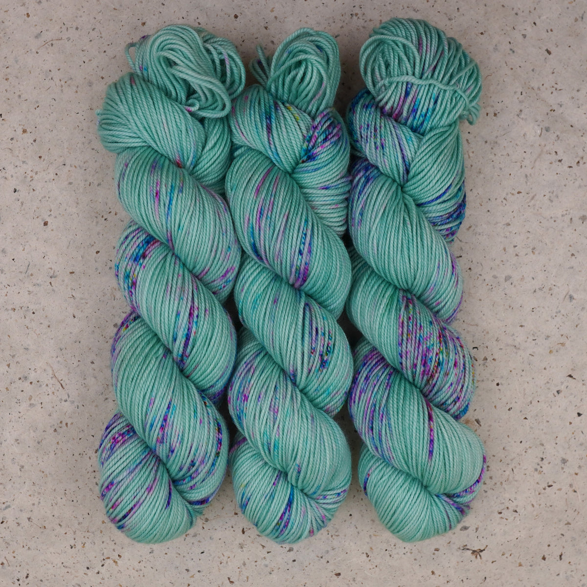 Wild Woollys Undersea Garden DK yarn, three skeins in soft mint green with purple and blue speckles