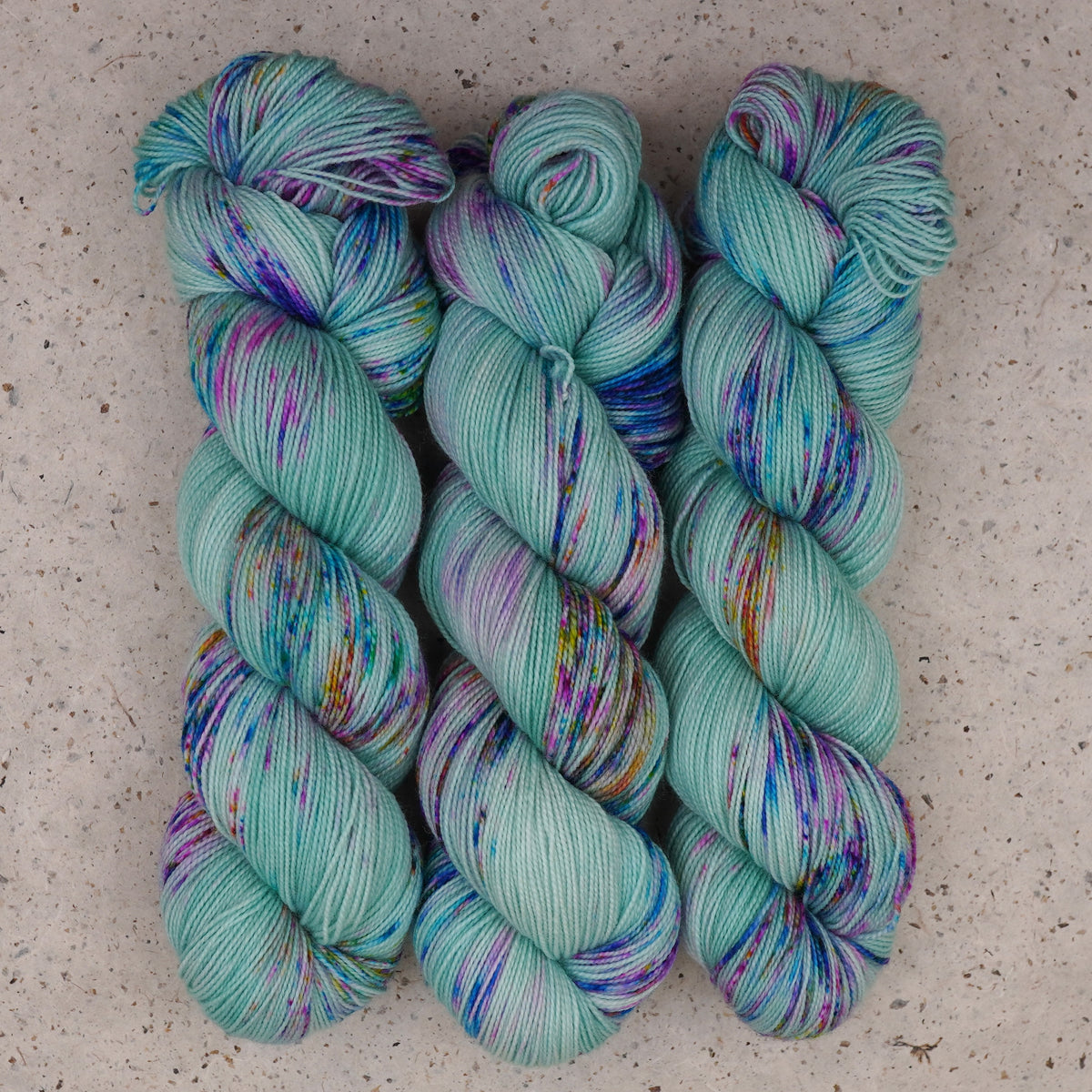 Wild Woollys Undersea Garden Fingering yarn, three skeins in soft mint green with purple and blue speckles