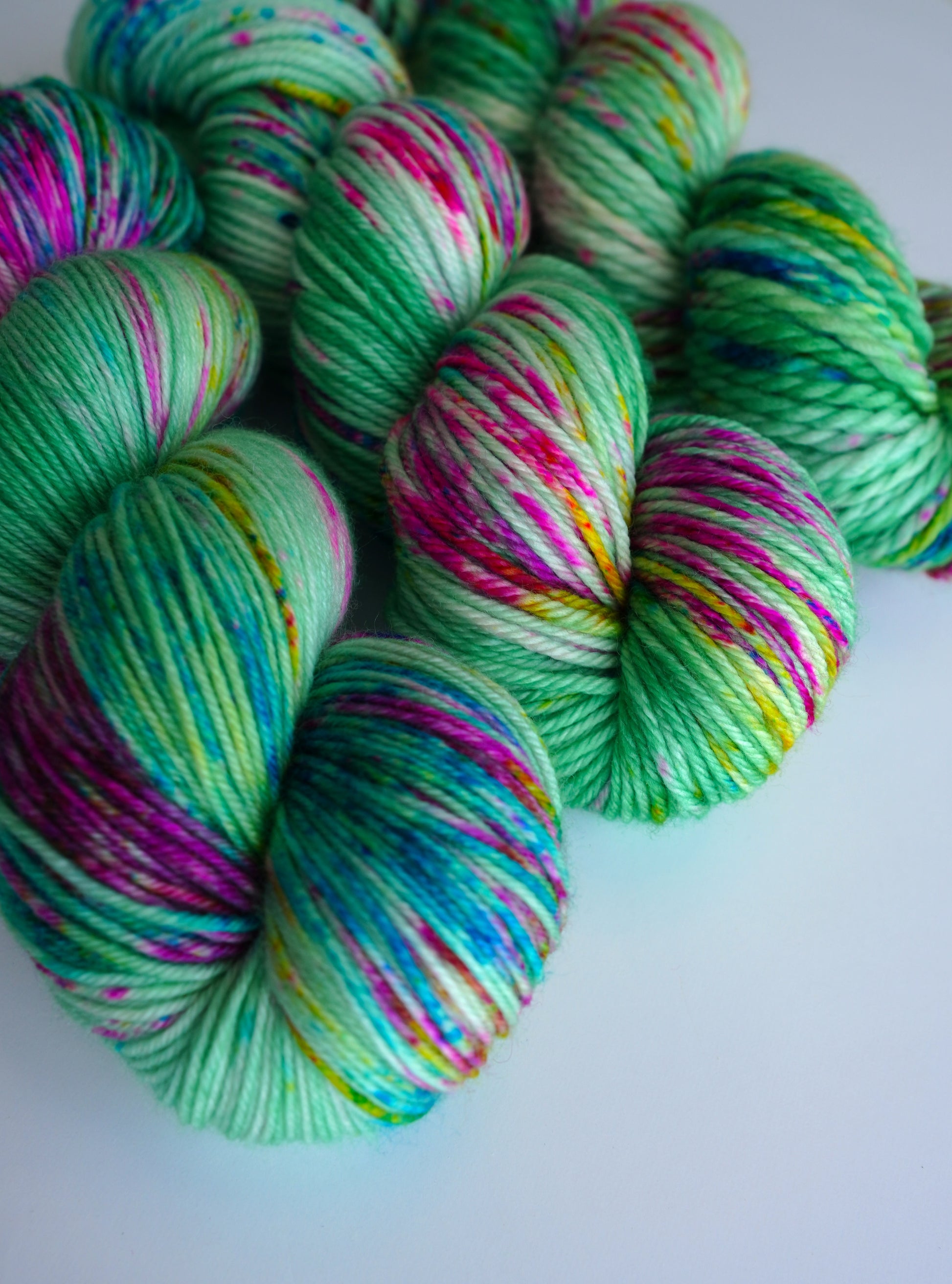 Colorful skeins of yarn with green, pink, and blue patterns on a white background.