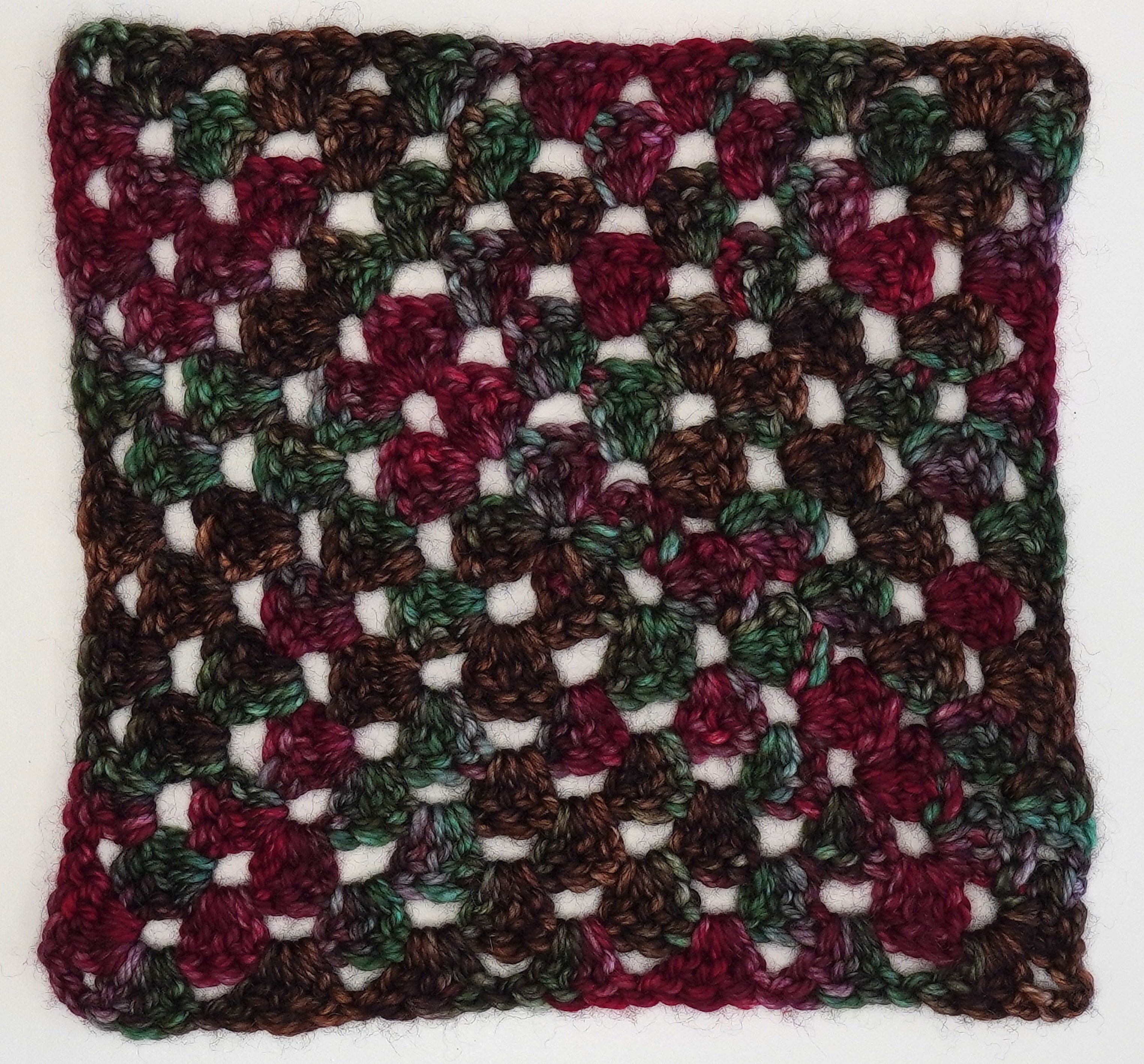 Woodland Christmas granny square by Wild Woollys, crocheted in variegated yarn with shades of green, brown, and red