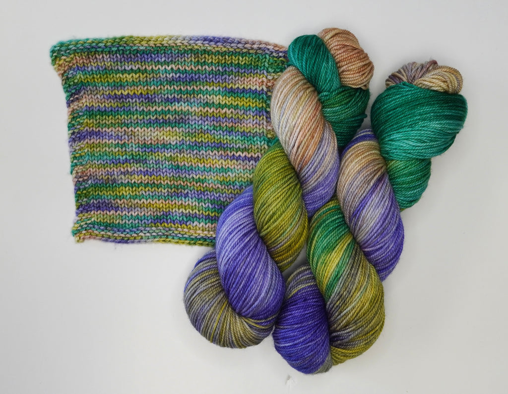 Water Lilies yarn by Wild Woollys, a skein of purple, green, and brown yarn with a knitted swatch