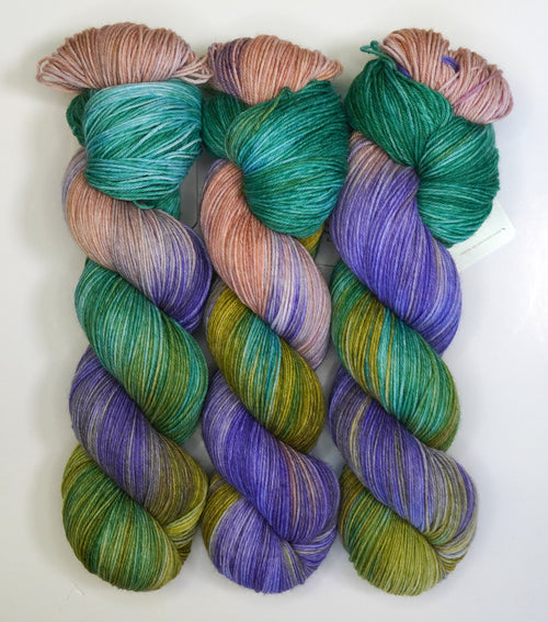 Three skeins of Wild Woollys Water Lilies yarn in shades of green, purple, and peach