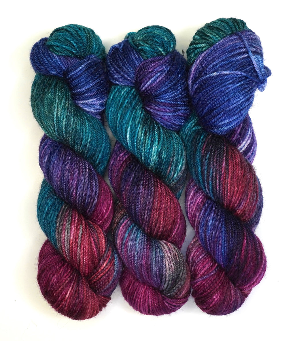 Three skeins of multicolored yarn in shades of blue, purple, and red on a white background.