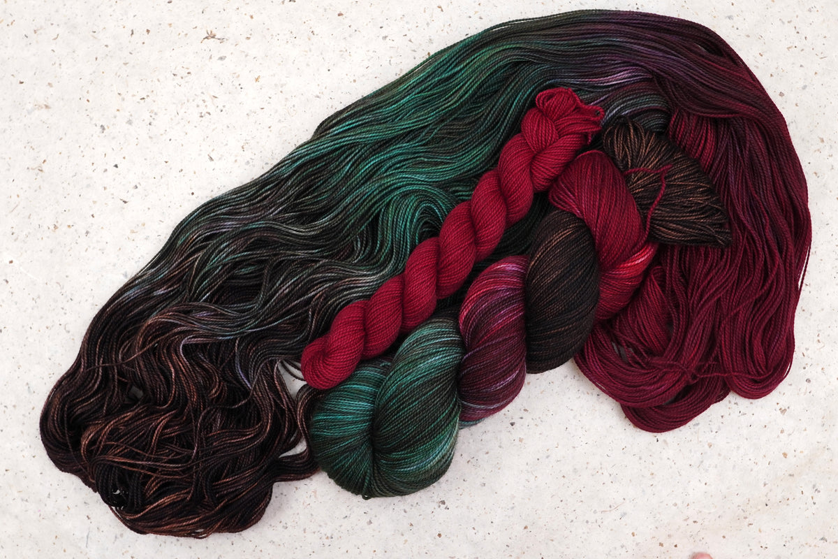 Wild Woollys Woodland Christmas sock set, an unwound skein in deep forest green, crimson, and near-black with a contrasting crimson mini-skein