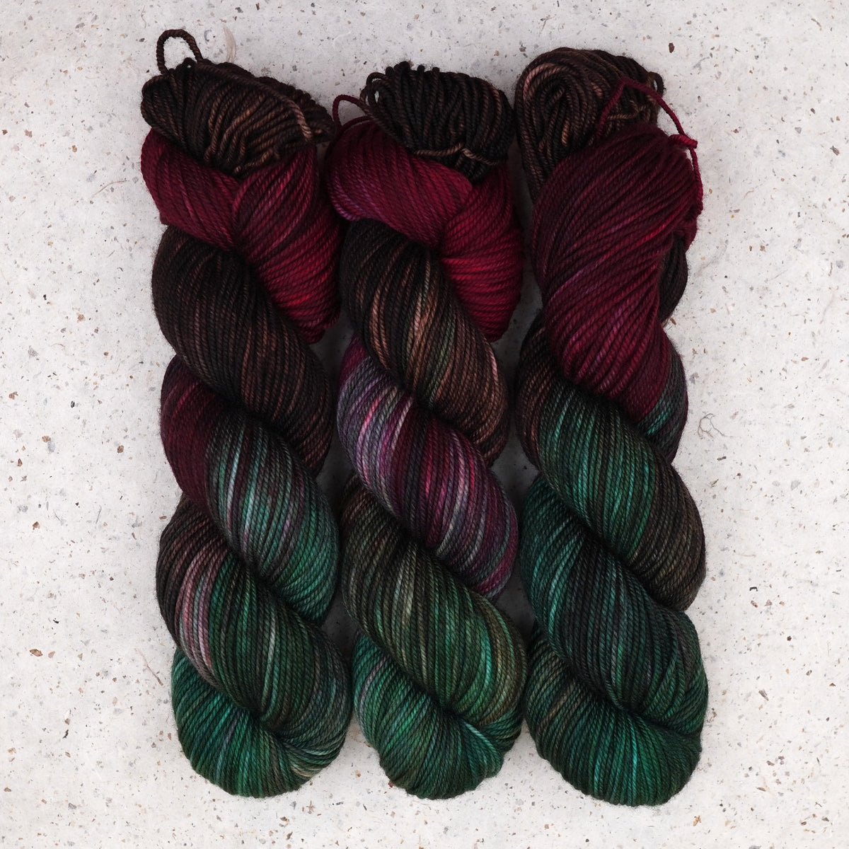 Wild Woollys Woodland Christmas DK yarn, three skeins in deep forest green, crimson, and near-black