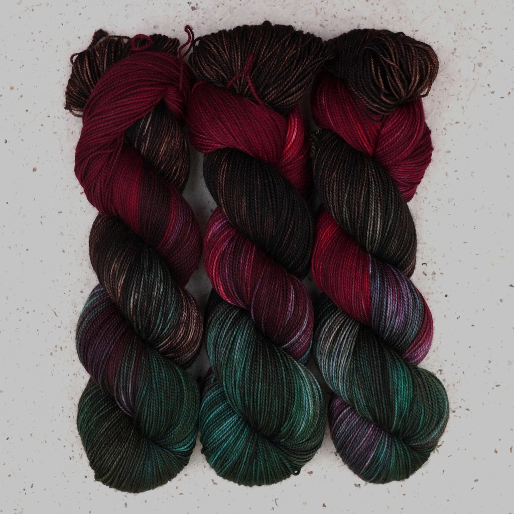 Wild Woollys Woodland Christmas Fingering yarn, three skeins in deep forest green, crimson, and near-black