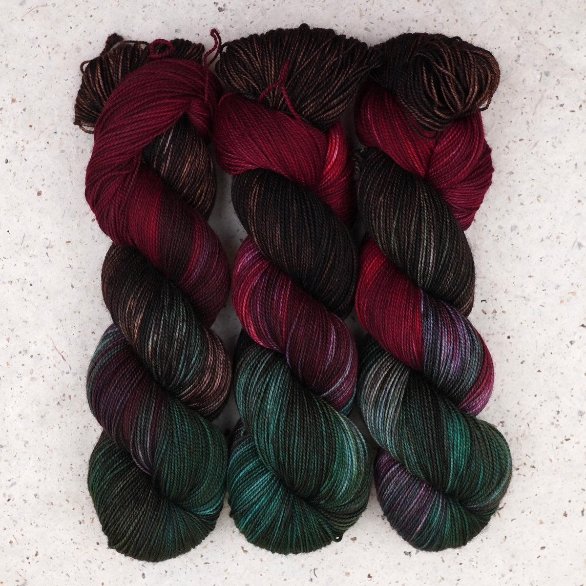 Wild Woollys Woodland Christmas Fingering yarn, three skeins in deep forest green, crimson, and near-black